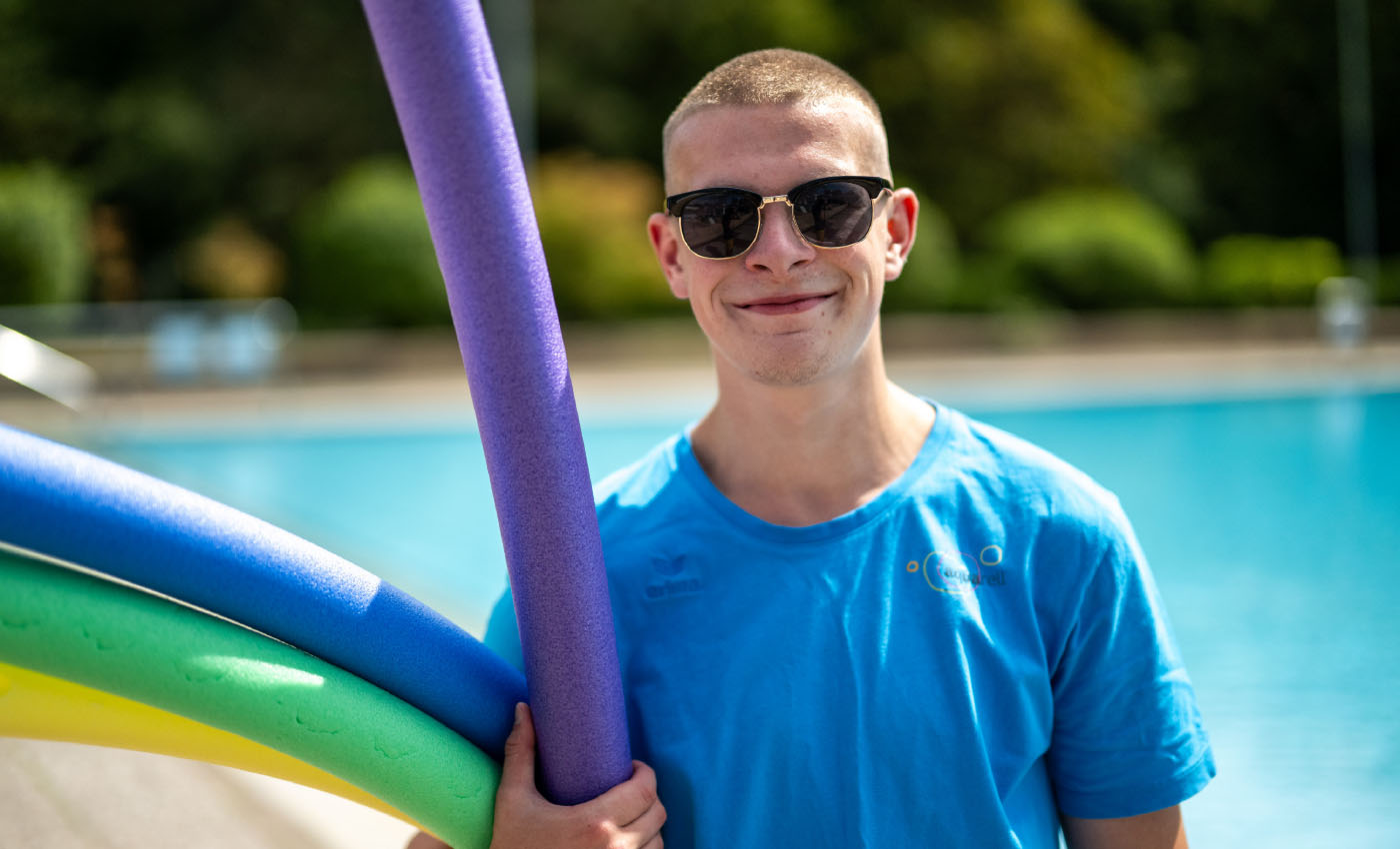 Der Mitarbeiter des Freizeitbads Aquarell, Aaron, lächelt mit Sonnenbrille in die Kamera
