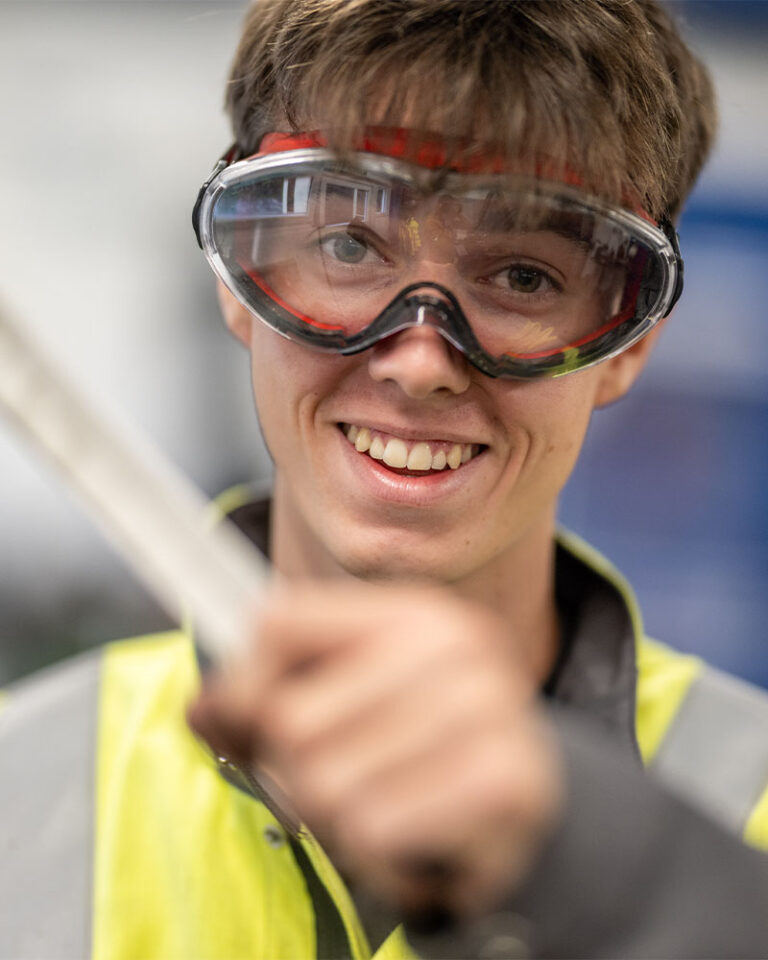 Auszubildender (Metallbauer) Robby Tappe hält lächelnd Arbeitswerkzeug in die Kamera